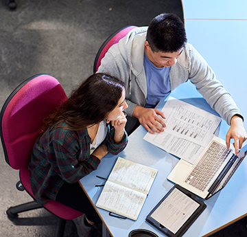 Two people sitting at a desk and looking at books