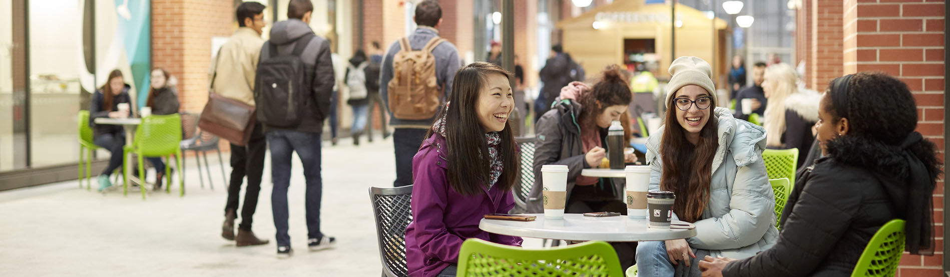 Three female students sitting around a table talking and drinking coffee