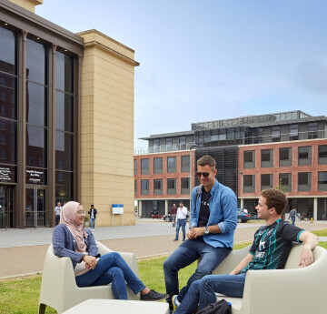 Three students sitting outside at Bay Campus. It is a sunny day.