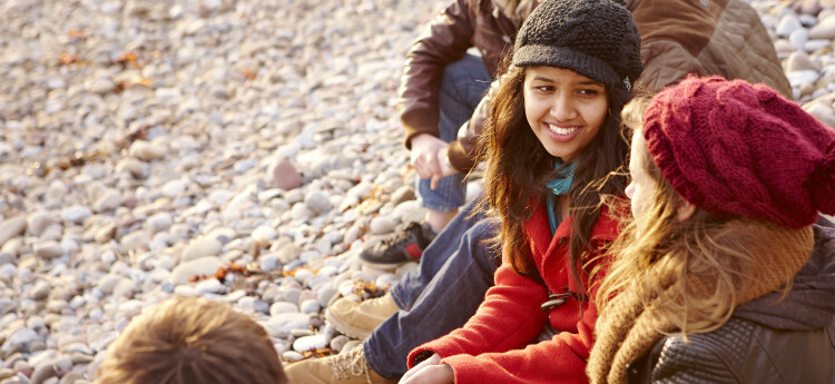 Four students sitting on a pebble beach, talking to each other. 