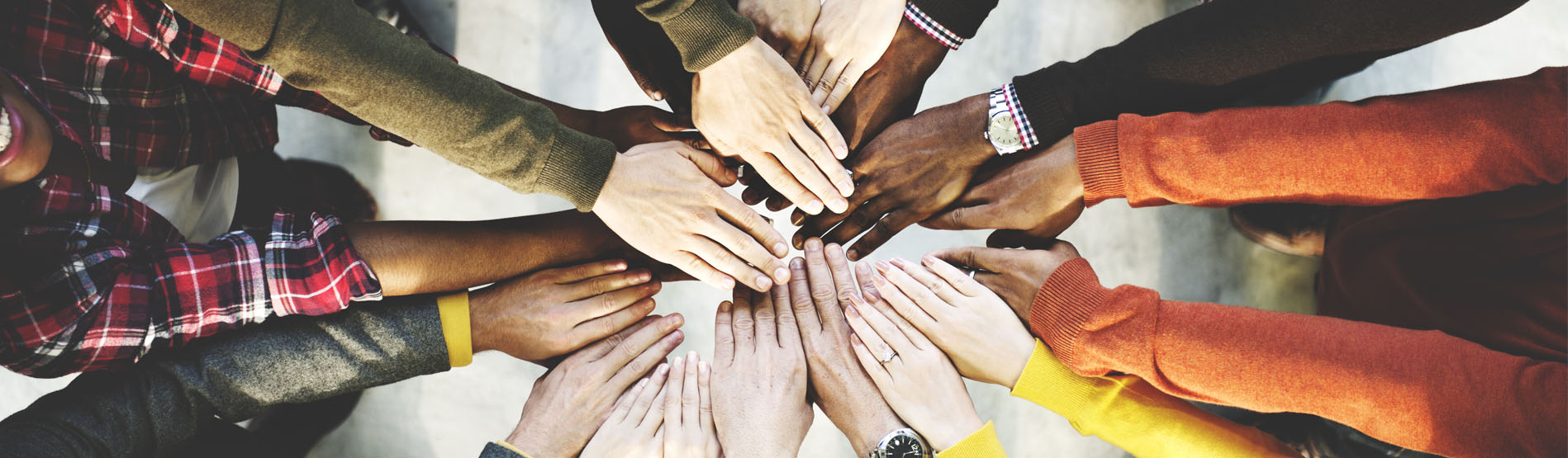 Aerial photo of group of people standing in a circle placing their hands together in the middle 